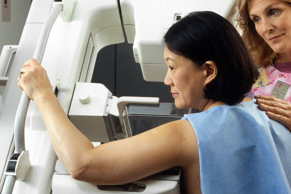 Woman in hospital gown standing up against a mammogram machine.