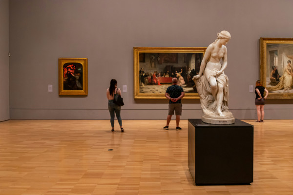 People looking at art in an art gallery with a Greek statue in the foreground.