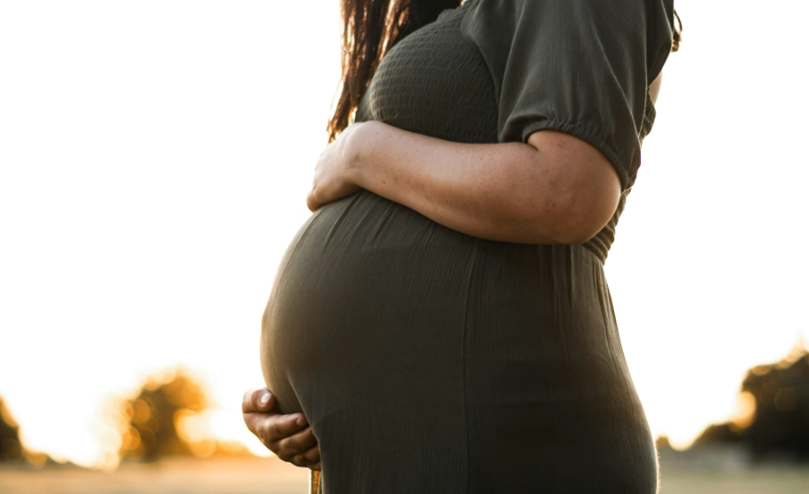 Woman in green dress holds her pregnant belly.
