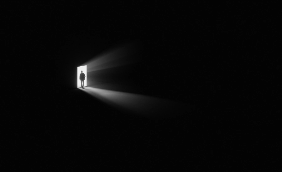 All black image, just the silhuoette of a person standing in front of an open door.